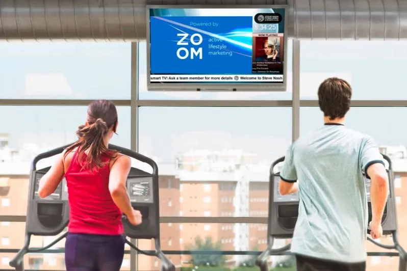 Spordiklubi liikmed kardiomasinatel seinal oleva ekraani all